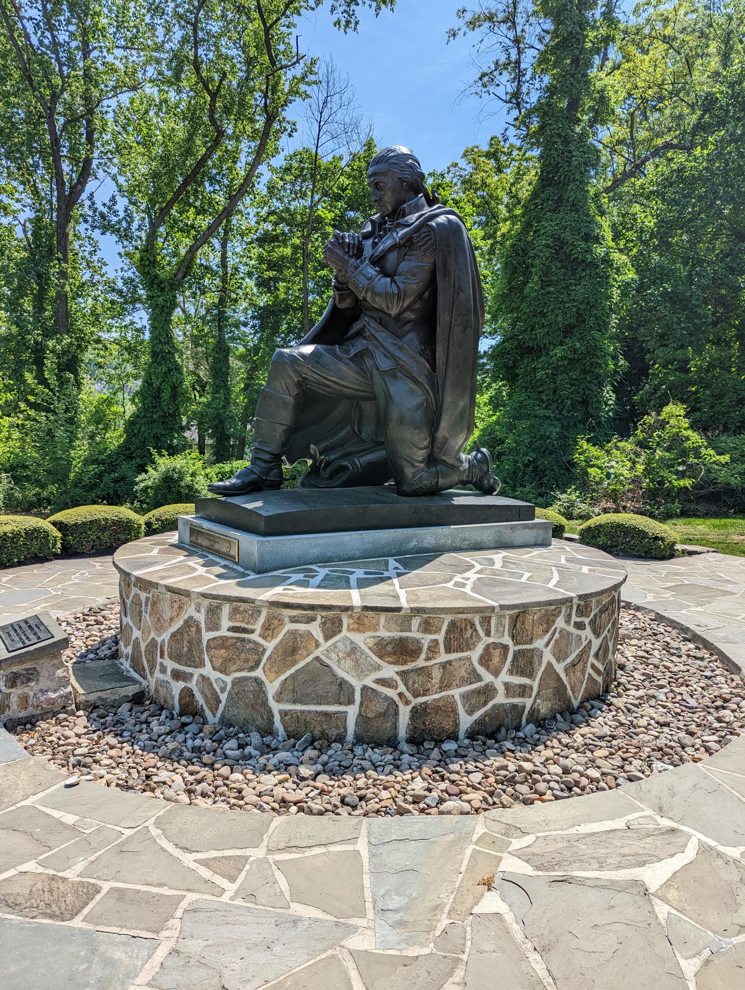 Side view of statue depicting George Washington at prayer with gardens surrounding the statue.