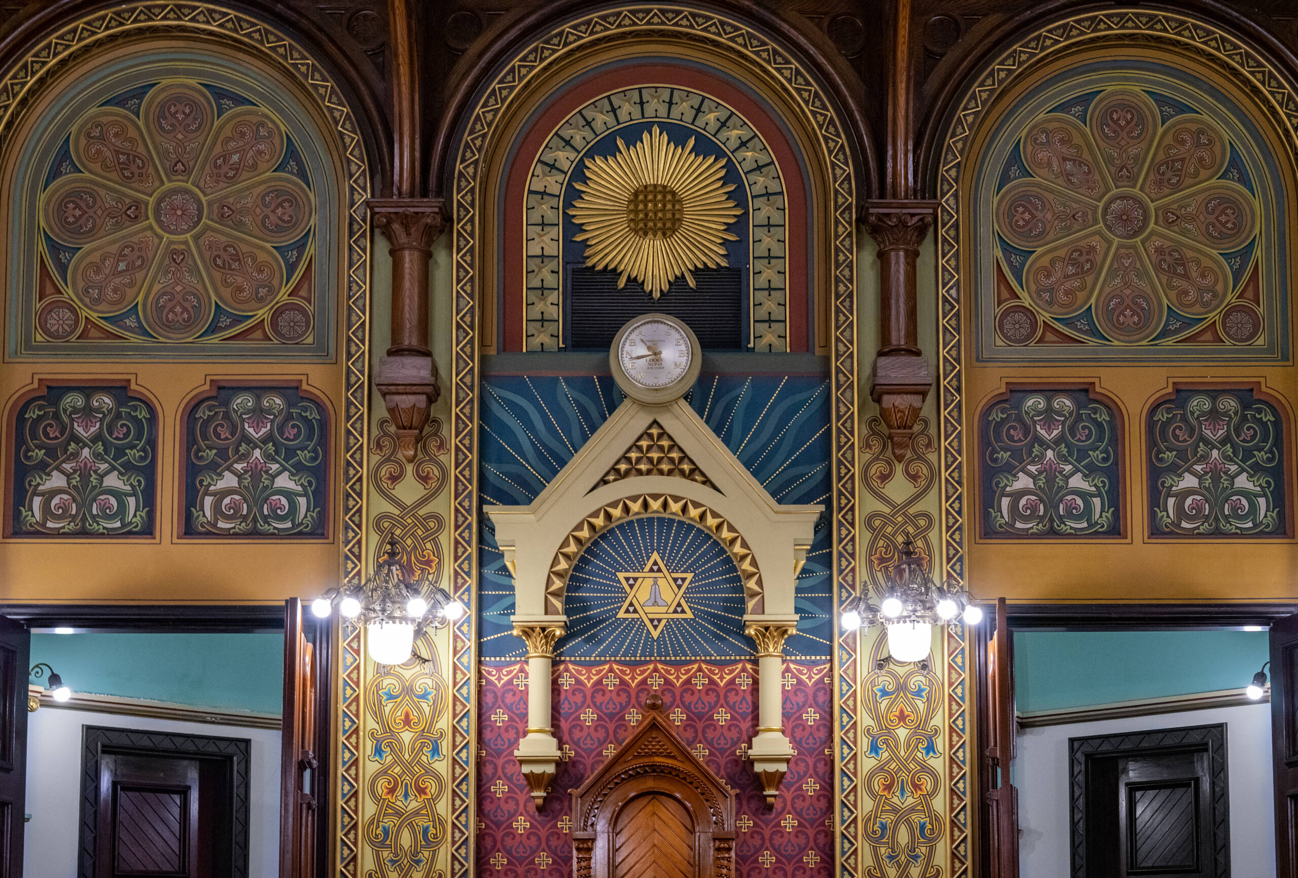 Ornate wall with blue, gold and red accents, the top of two doorways is visible.