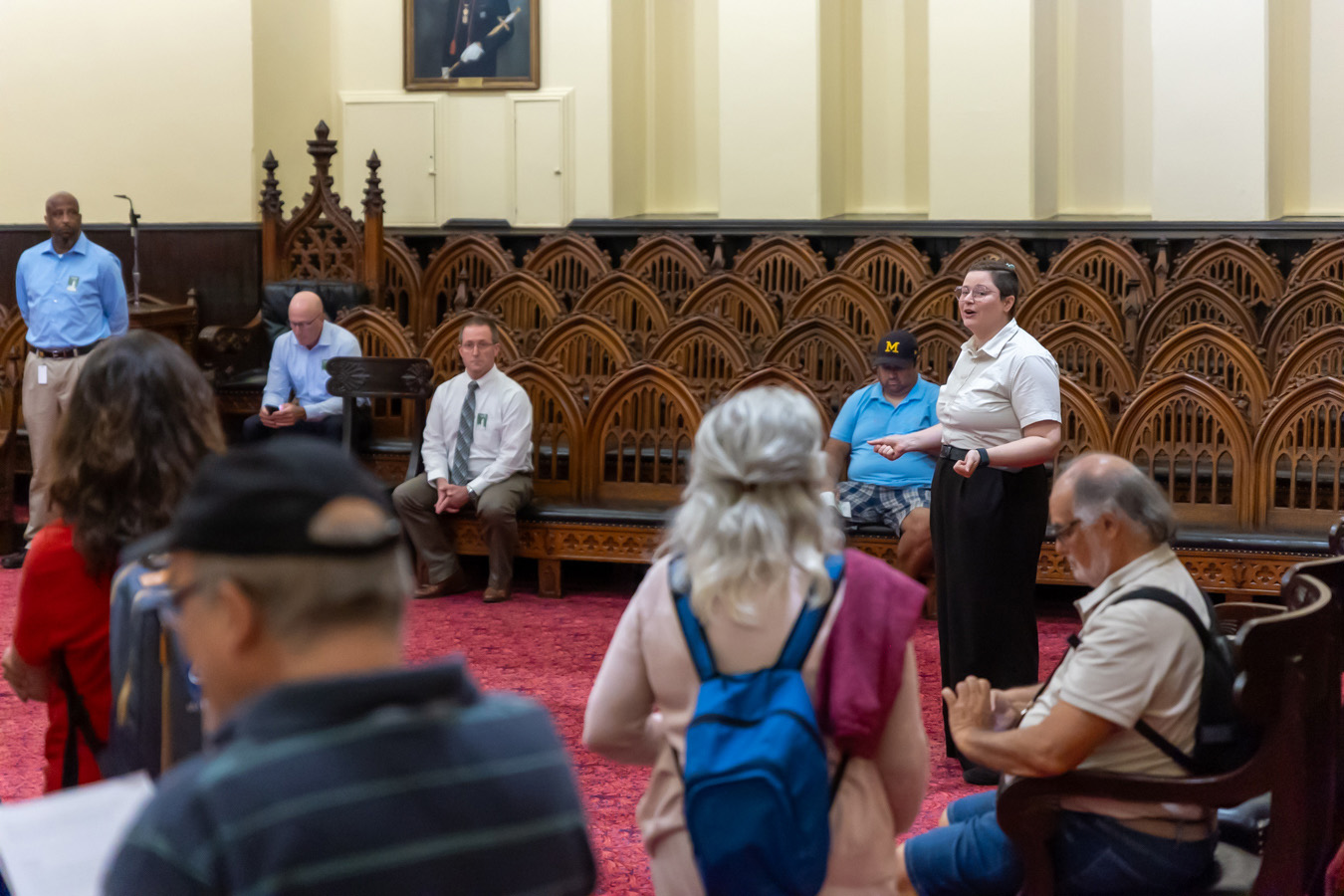 Tour guide speaking to group in lodge room with red carpet and white and wood walls